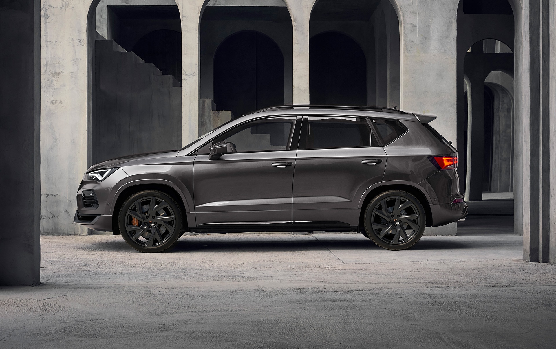 Boczna część CUPRY Ateca na tle betonowej budowli. Dobrze widoczne muskularne proporcje SUV-a. 