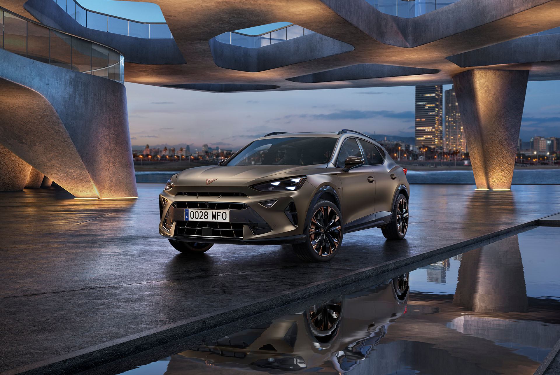 CUPRA Formentor 2024 Century Bronze Matt 2024 zaparkowana na nadmorskiej promenadzie. Sportowy i aerodynamiczny nowy samochód jest umieszczony w środkowej części kadru. Sceneria obejmuje futurystyczną architekturę oraz rozświetloną panoramę Barcelony o zmierzchu.