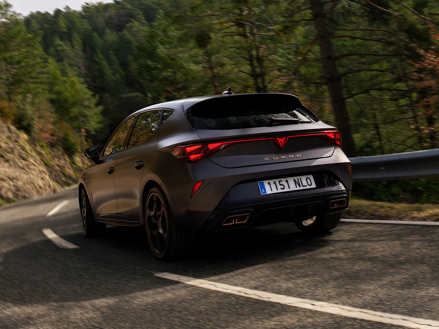 Ujęcie od tyłu: CUPRA Leon przemierza drogę w otoczeniu drzew.