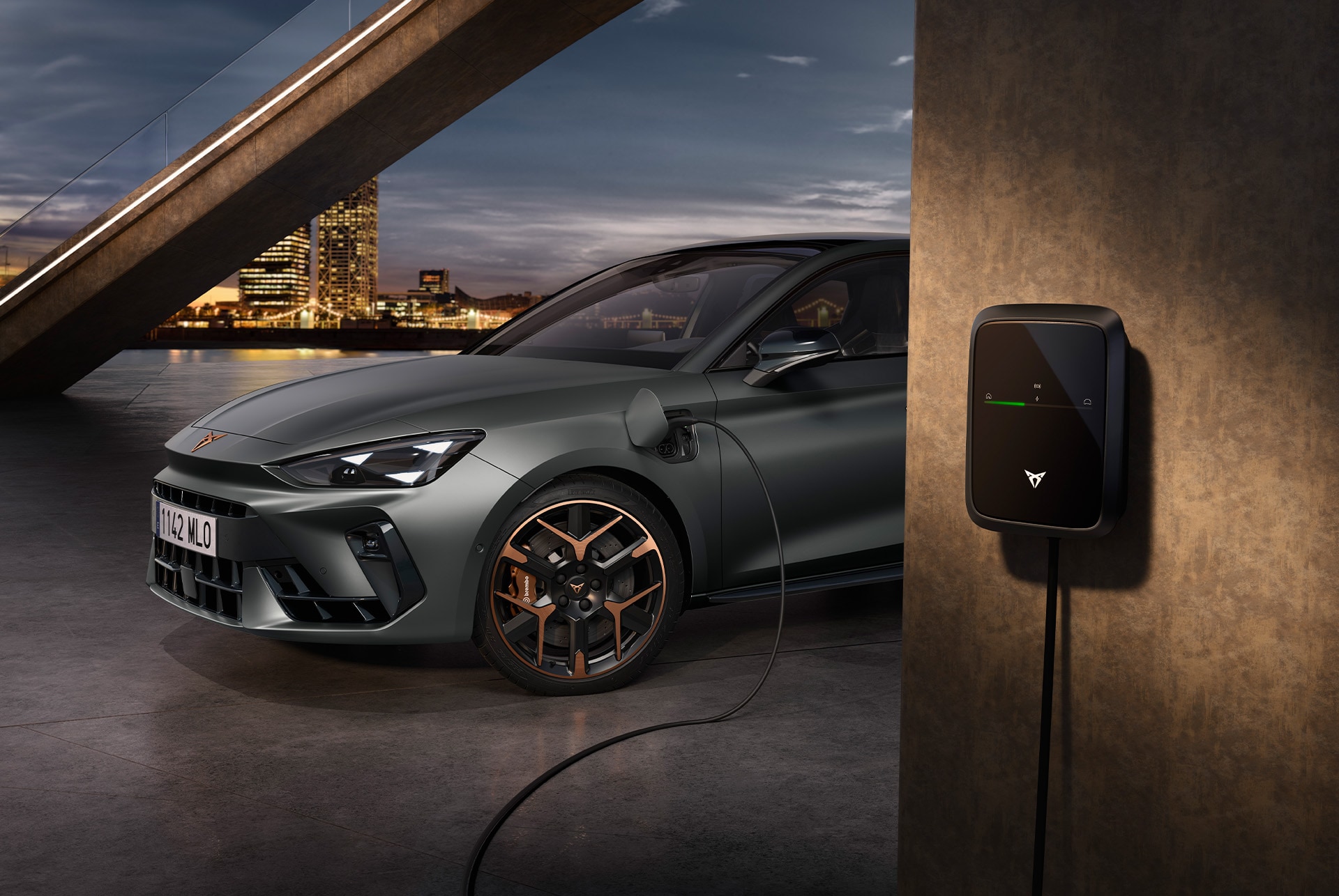 Ujęcie z boku przedstawiające samochód CUPRA Leon Sportstourer VZ e-hybrid podłączony do ładowarki na tle miejskiej scenerii.