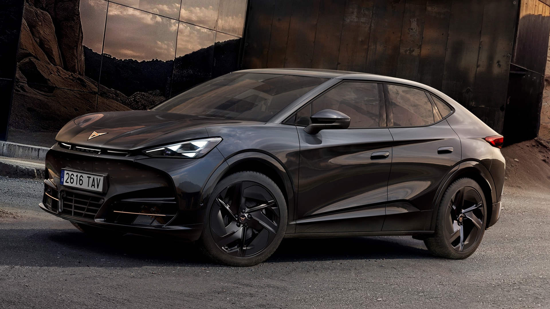 Efektowne ujęcie, widok 3/4 z przodu na model CUPRA Tavascan Black Edition zaparkowany w skalistej scenerii, prezentujący detale nadwozia, takie jak 21-calowe obręcze kół ze stopów lekkich Katla w kolorze czarnym.