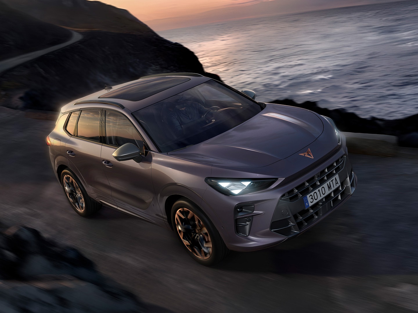 CUPRA Terramar z systemem Dynamic Chassis Control (DCC) jadąca wzdłuż nadmorskiej drogi, prezentując lakier Dark Void oraz 20-calowe felgi Hadron Copper.