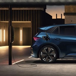 Samochód elektryczna CUPRA Leon ładowana na parkingu przez ładowarką ścienną, oświetlene otoczenie