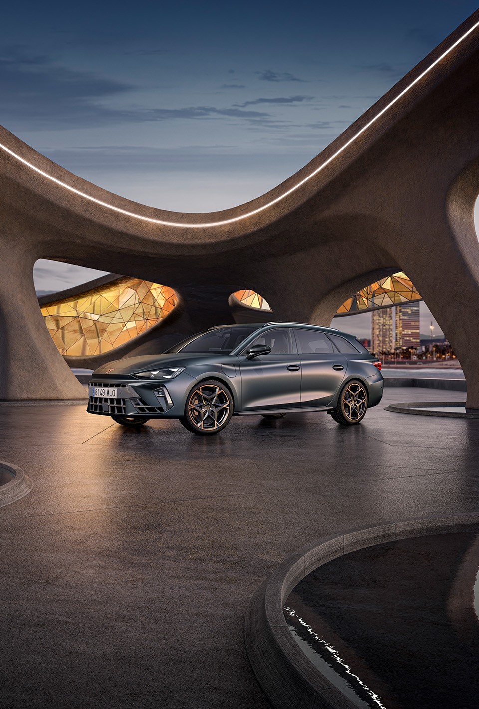 Szerokokątny widok na nowy, sportowy pojazd hybrydowy CUPRA Leon Sportstourer 2024 w kolorze Grey Matte zaparkowany w miejskiej scenerii, przed dużymi geometrycznymi oknami inspirowanymi gaudim.